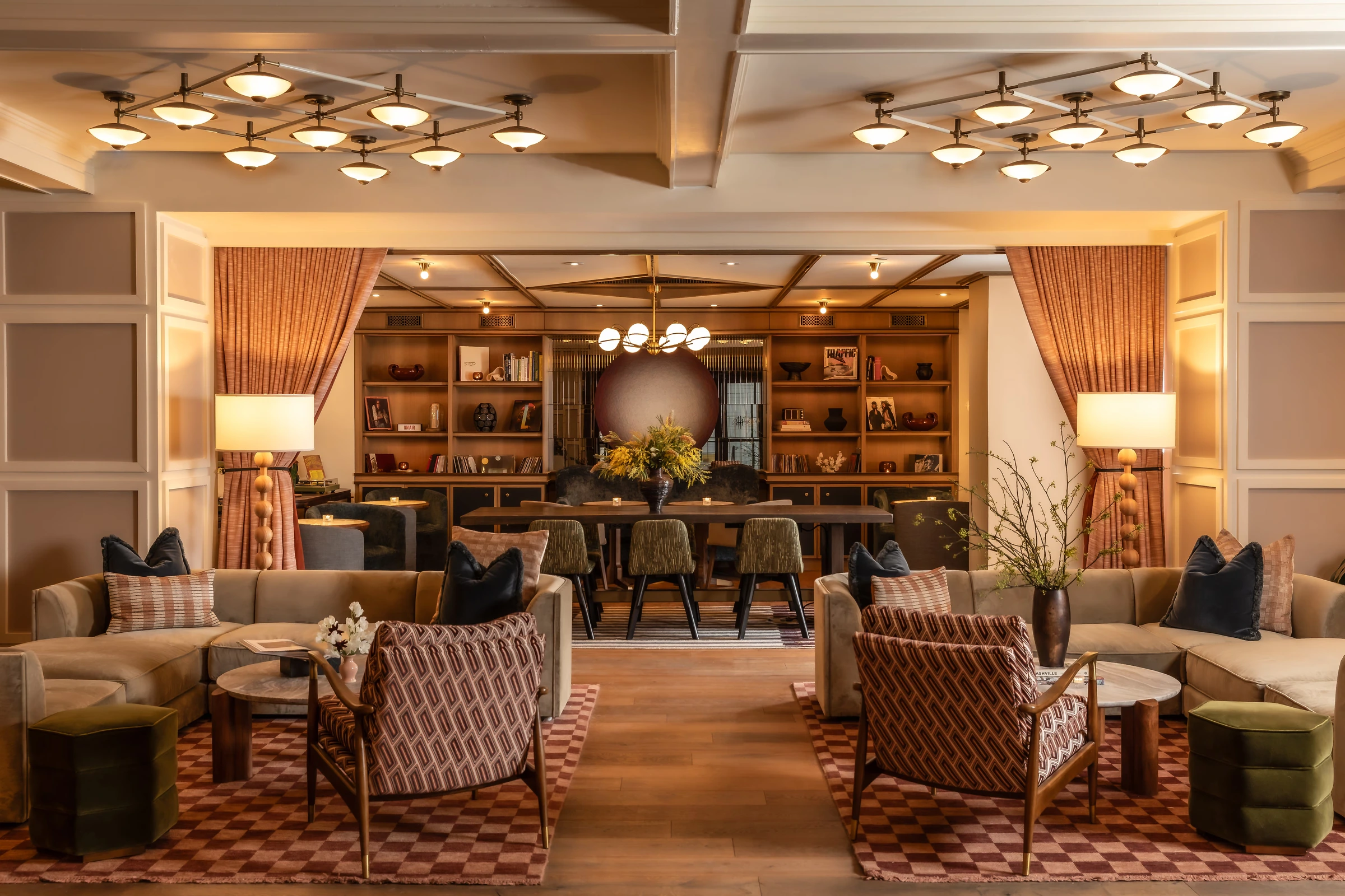 A hotel lobby lit by decorative ceiling fixtures, pendants and table lamps